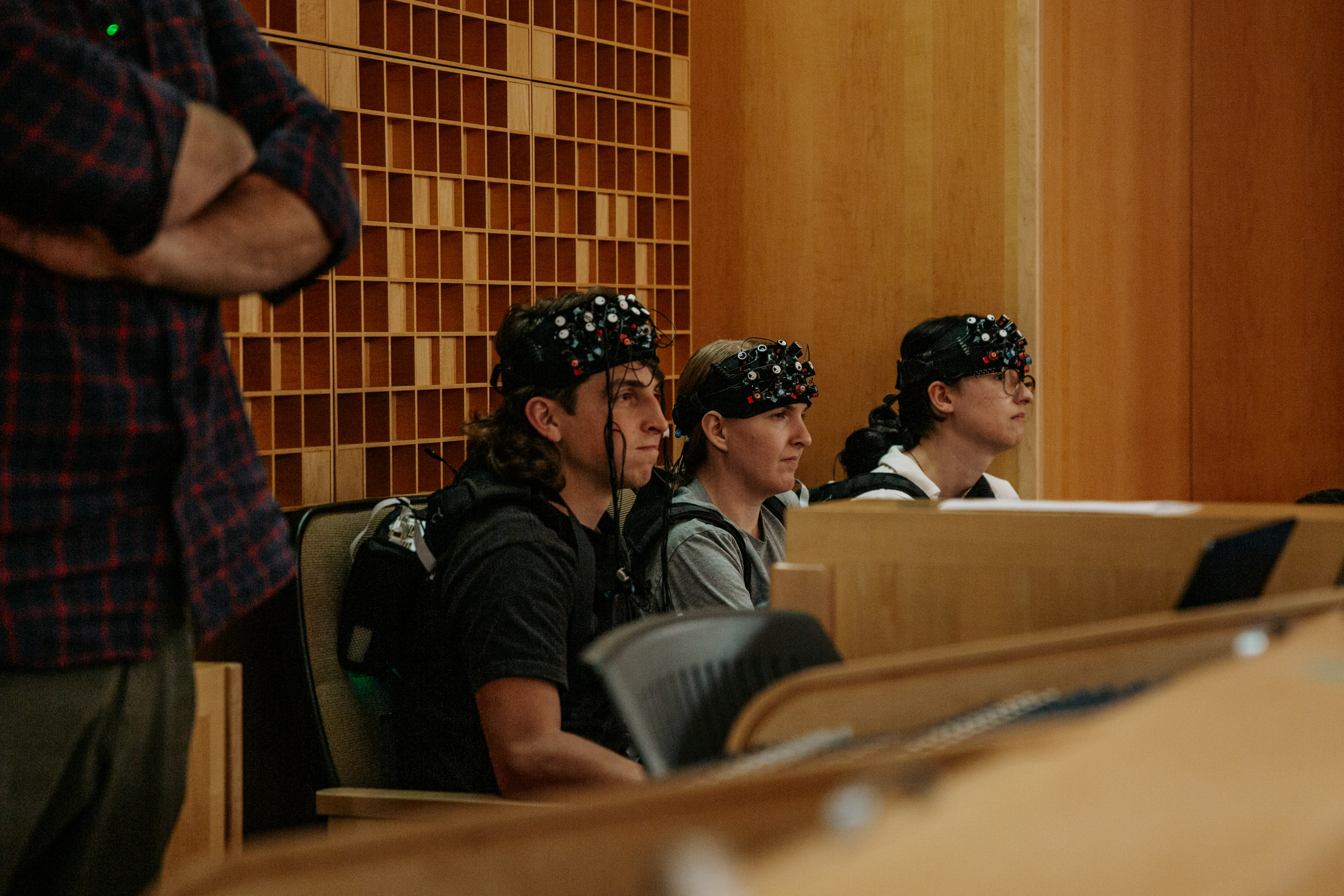Three audience members wear equipment to monitor and record brain activity.