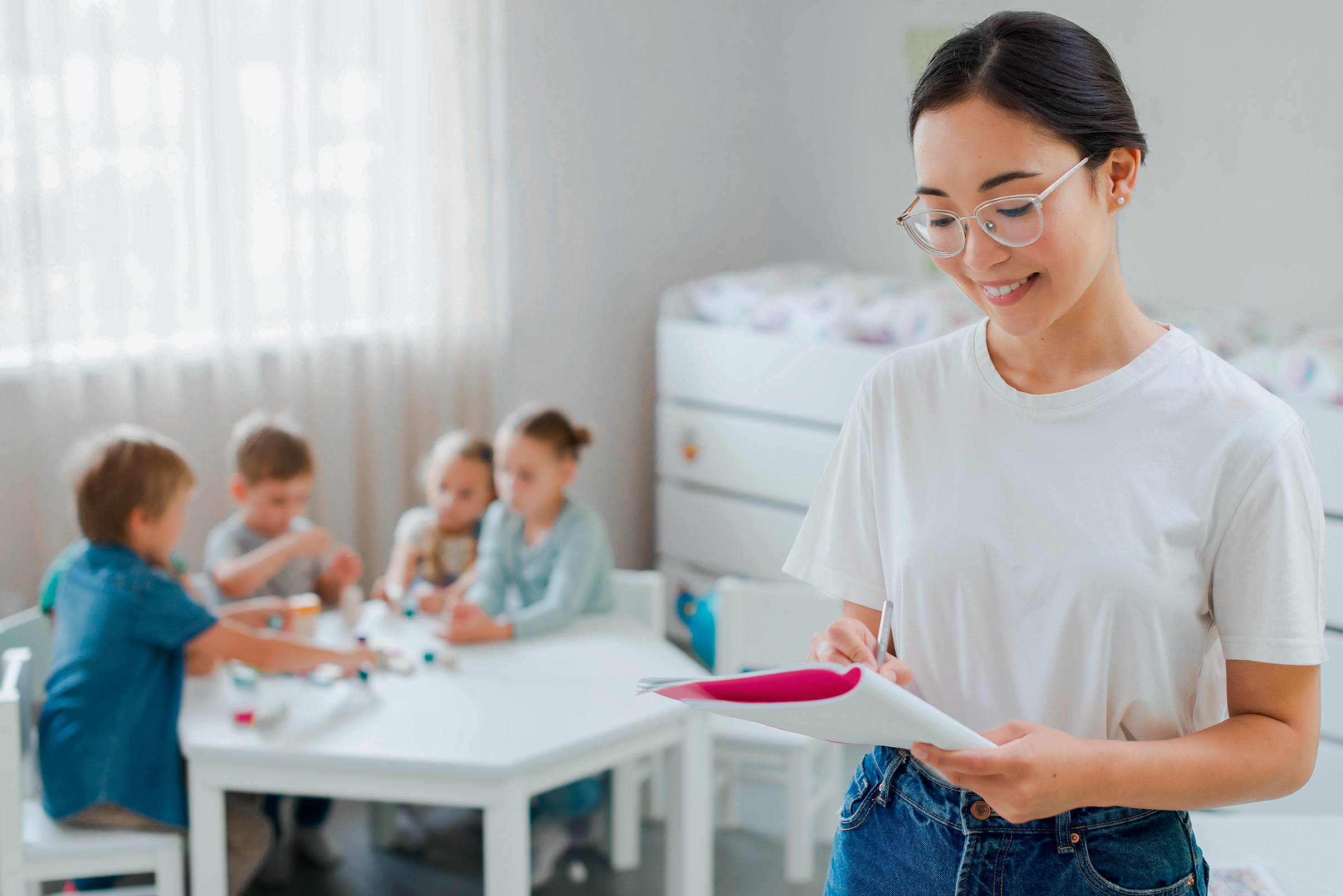Girl writing in notebook with children at table in background