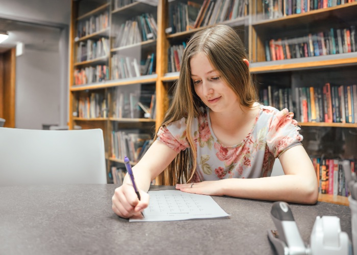 Student writing on paper in library